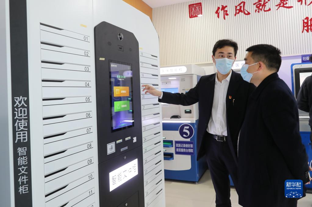上海市闵行区七宝镇社区事务受理服务中心的工作人员(左)向前来办事的居民介绍智能文件柜的使用方法(2021年3月3日摄)。新华社记者 方喆 摄